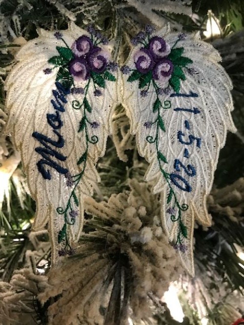 Decorative angel wings ornament with floral details and embroidered text on a Christmas tree.